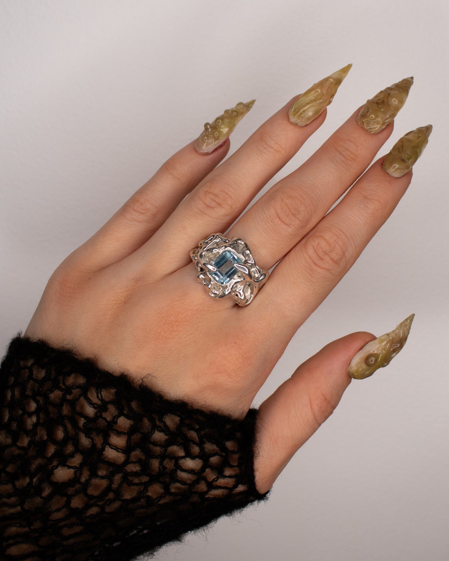 Hand wearing a decorative ring with a blue gemstone on a plain background
